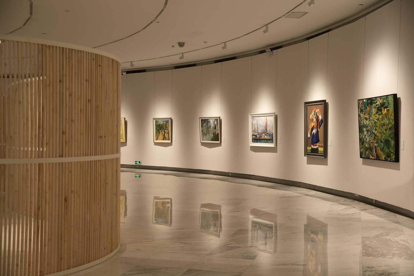 图片展示了一个画廊内部，墙上挂着多幅画作，画廊地面反射着灯光，空间宽敞，有一面弯曲的木质隔断。