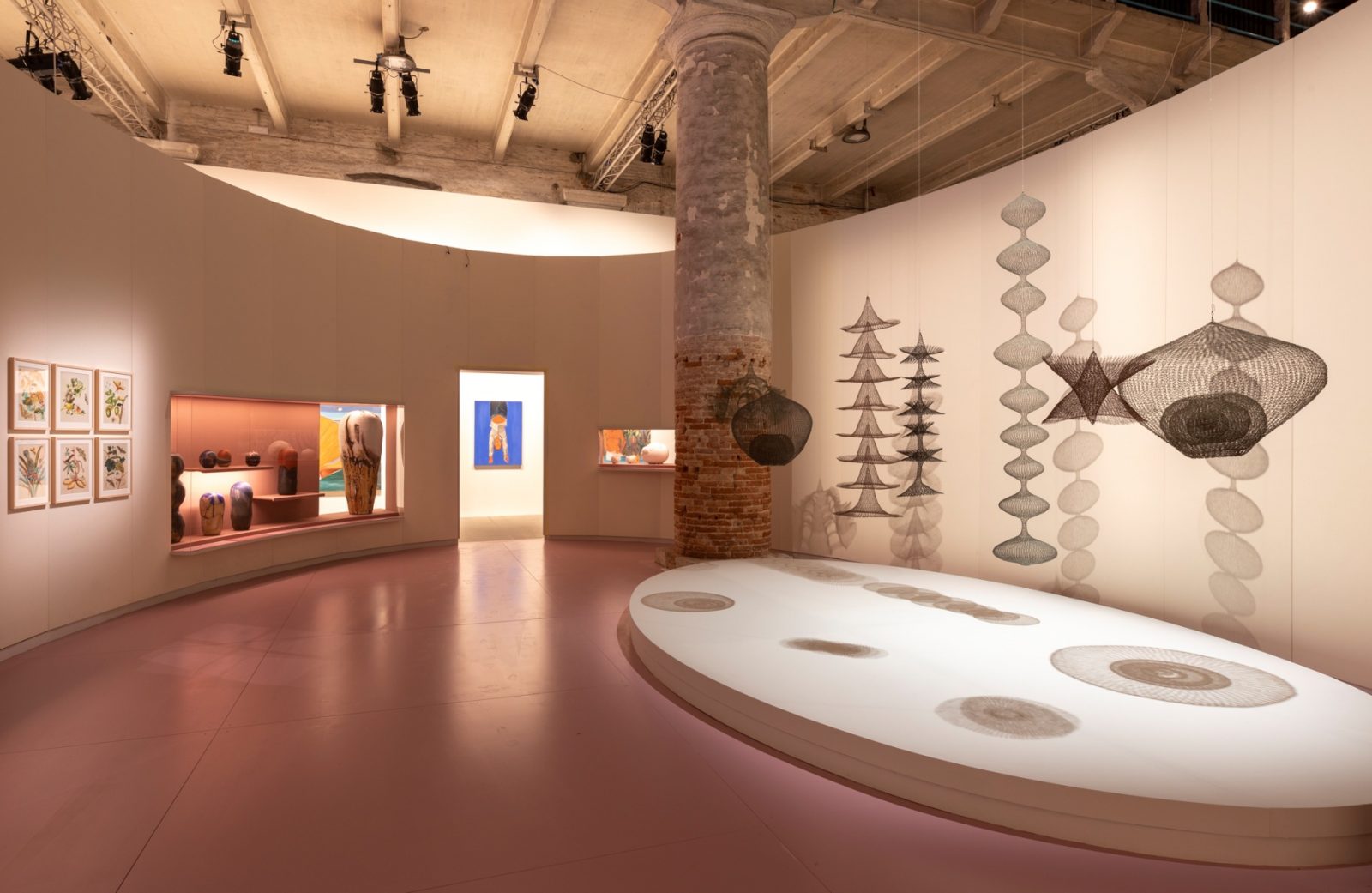 这是一间展览厅内部，墙上挂着不同风格的艺术作品，还有几件立体艺术品陈列在地面和台子上。