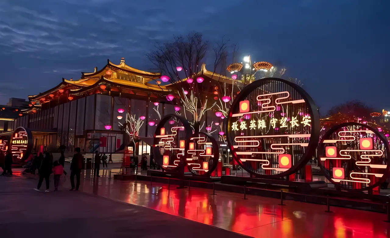 图片展示了夜幕下装饰华丽的灯光节，传统建筑旁巨大的灯笼和彩灯，人们在观赏，节日氛围浓厚。