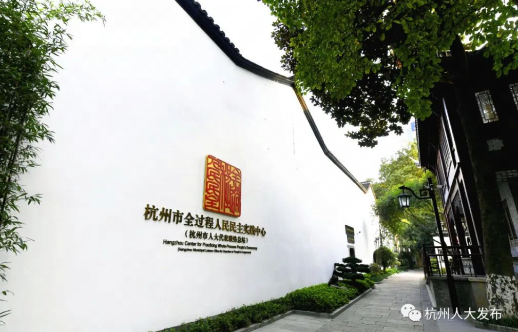 这是一幅展示中国传统建筑风格的图片，有着弯曲的屋顶、洁白的墙面和一块红色的牌匾，周围绿树成荫。