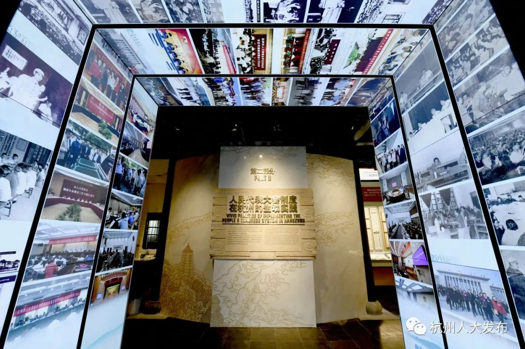图片展示了一个展览空间，墙面和天花板贴满了黑白及彩色照片，中央有介绍文字的展板。