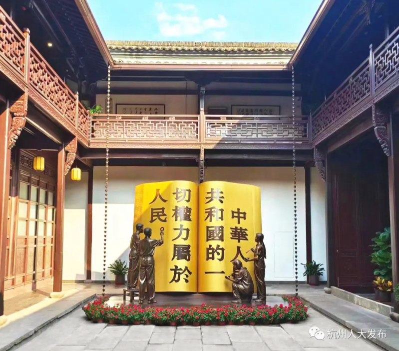 这是一座具有中国传统建筑风格的庭院，中间有一块大型金色牌匾，两侧是雕塑，周围装饰有绿植。