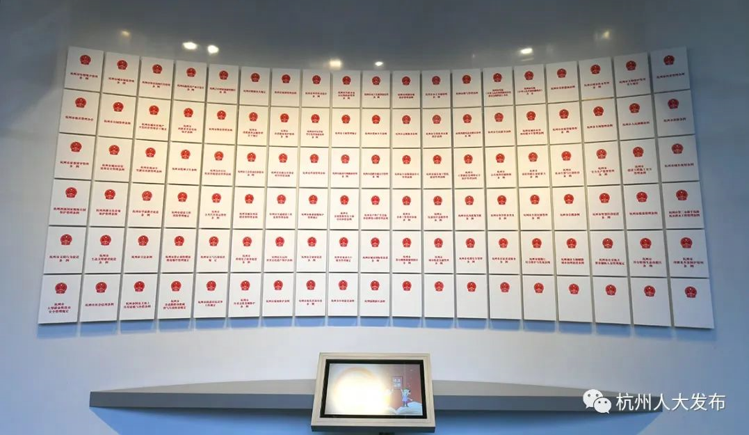图片展示了一面墙，上面挂满了排列整齐的红色徽章，下方有一台显示屏，整体给人一种庄重的博物馆展览感。