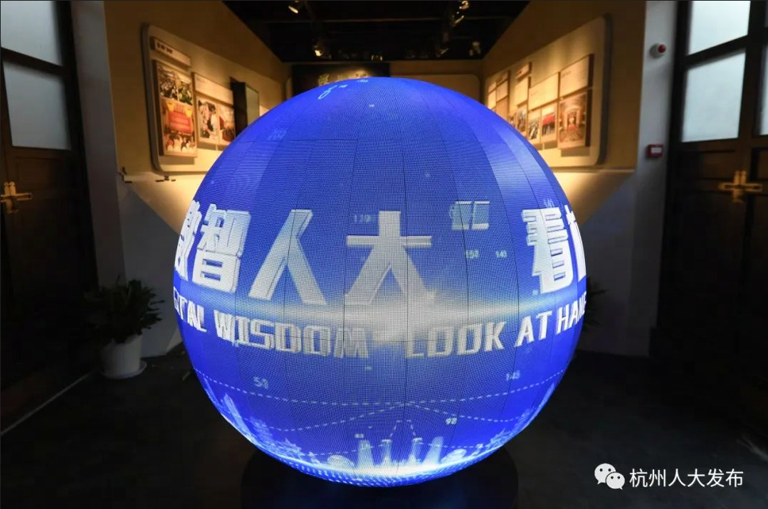 图片展示了一个巨大的蓝色球体，球体表面有文字：“智慧人大”和一些数字，背景是昏暗的展览厅。