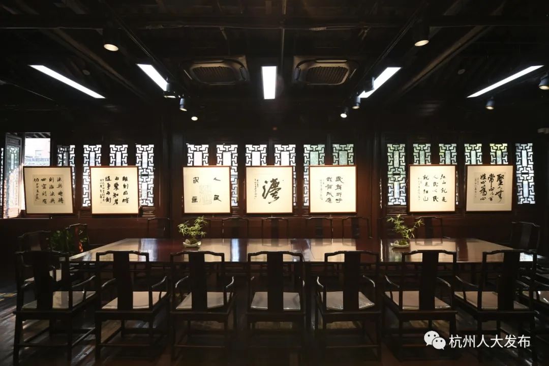 图片展示了一个中国书法展览室，墙上挂满了书法作品，前方摆放着排列整齐的桌椅，环境庄重典雅。