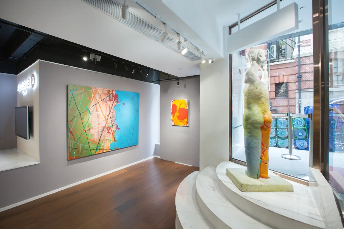 这是一家现代艺术画廊内部，墙上挂着几幅色彩鲜艳的抽象画作，中间展示着一尊抽象雕塑，环境优雅。
