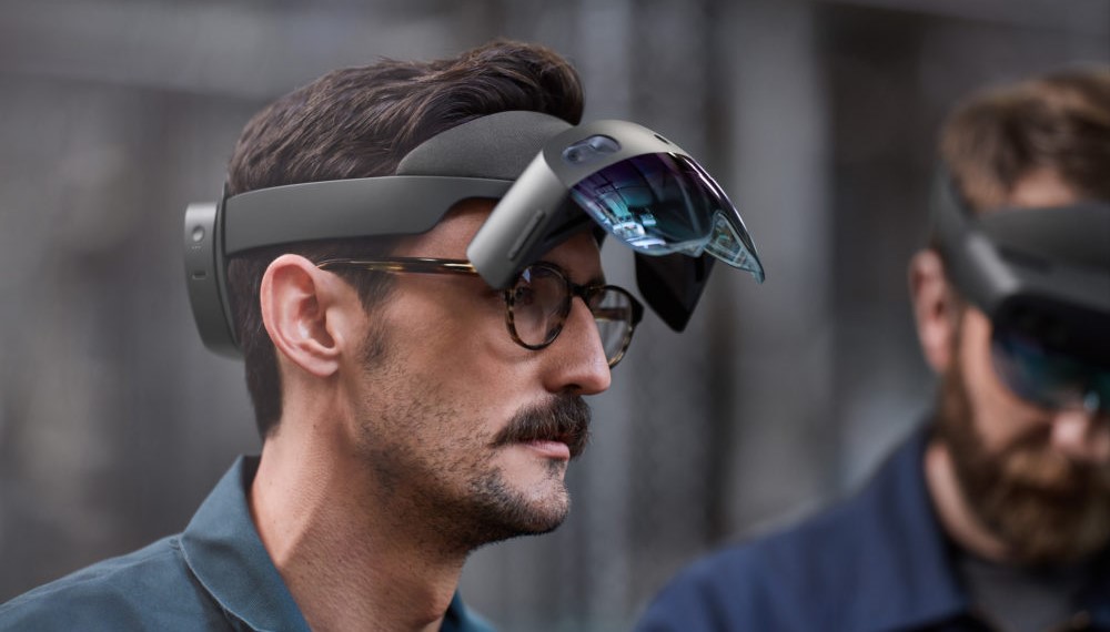 图片展示两位男性佩戴着先进的头戴式显示设备，似乎在体验增强现实或虚拟现实技术。
