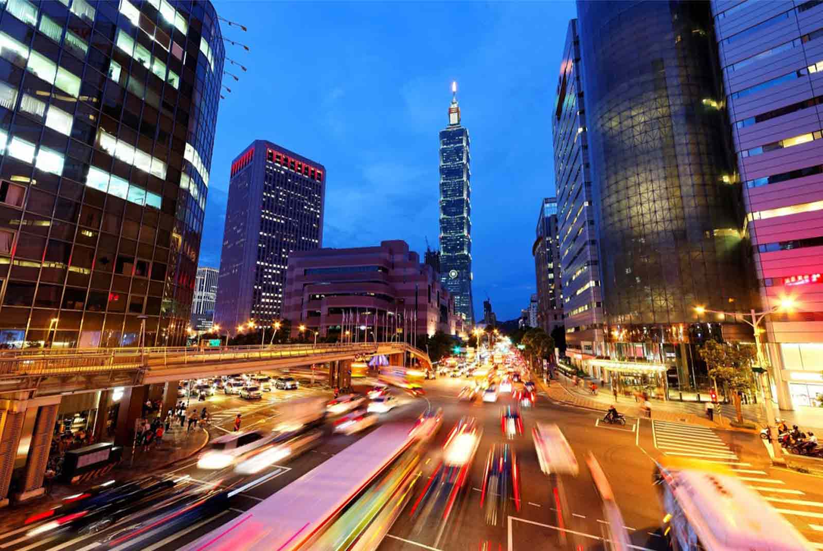 这是一张城市夜景照片，展示了繁忙的街道，车辆的长曝光轨迹，现代高楼大厦和夜幕下的灯光。