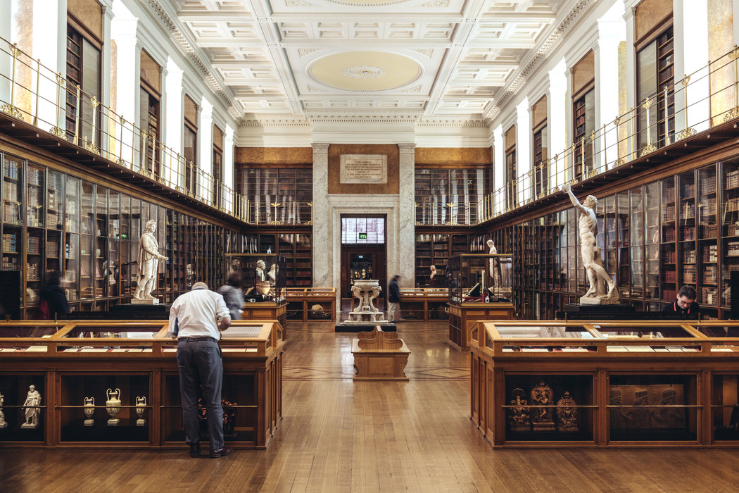 图片展示了一间装饰典雅的图书馆，内有书架、雕塑和正在阅读的人们，环境宁静而庄重。