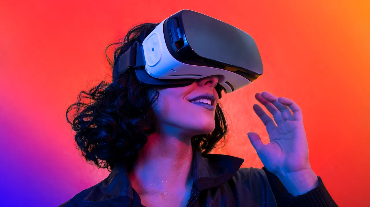 图片展示一位女士戴着虚拟现实头盔，似乎在体验虚拟世界，背景是红蓝渐变色，充满科技感。