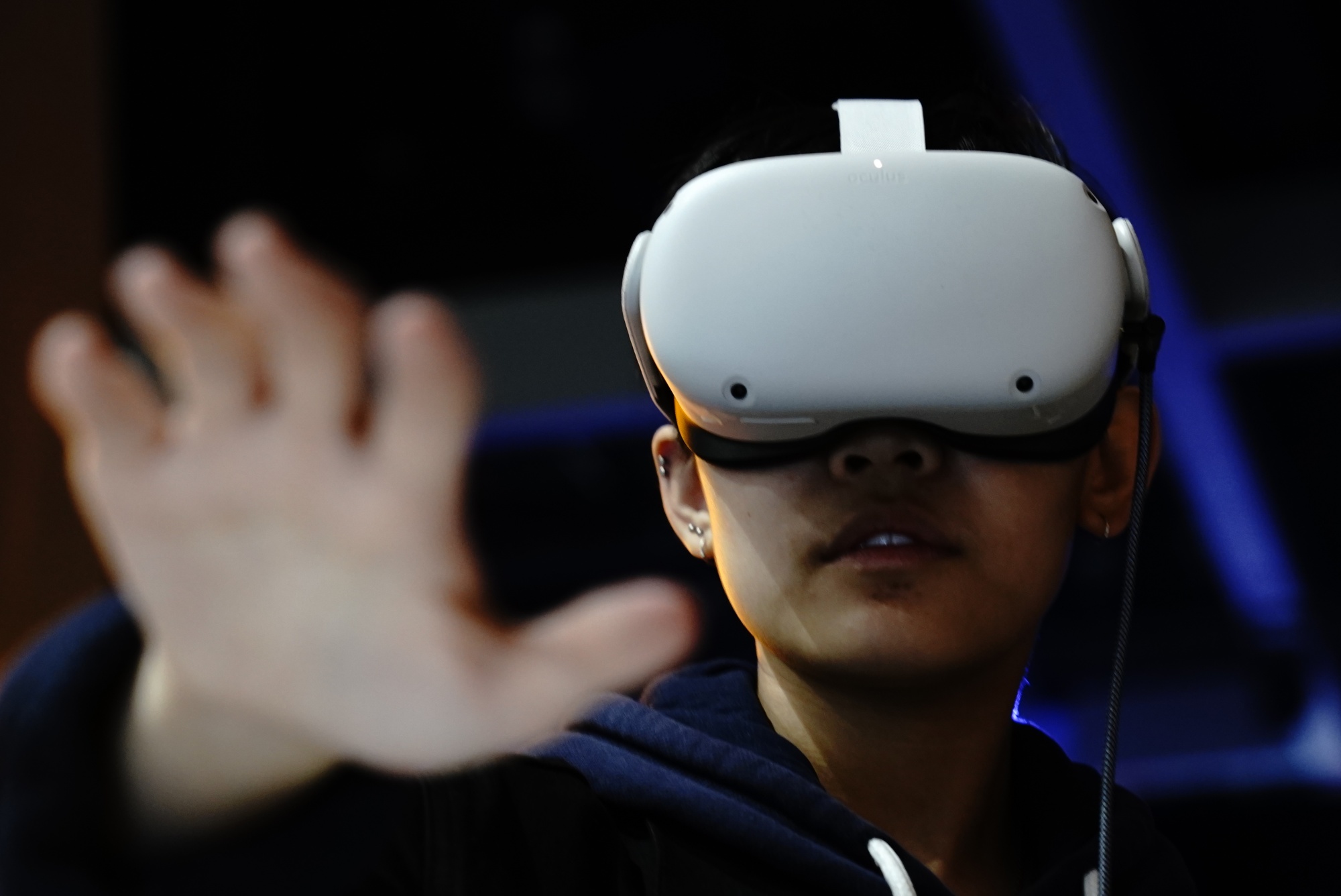 图片展示了一位戴着虚拟现实头盔的人，伸出手掌仿佛在触摸或操控虚拟世界中的物体。