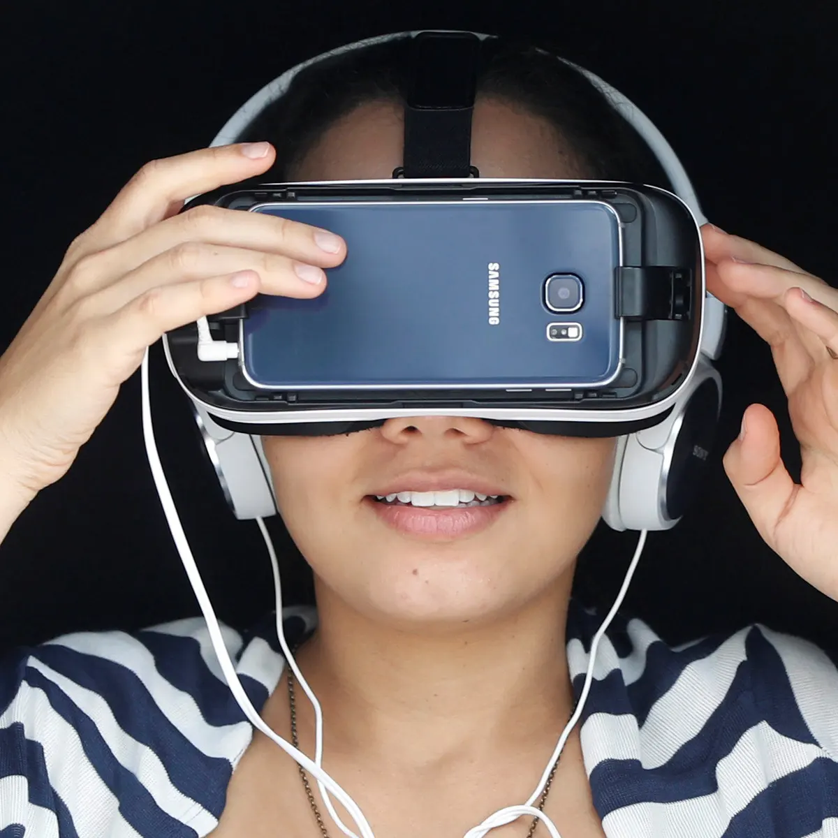 图片展示一位女性戴着虚拟现实头盔和耳机，似乎正在体验沉浸式的虚拟现实内容，背景为纯色。
