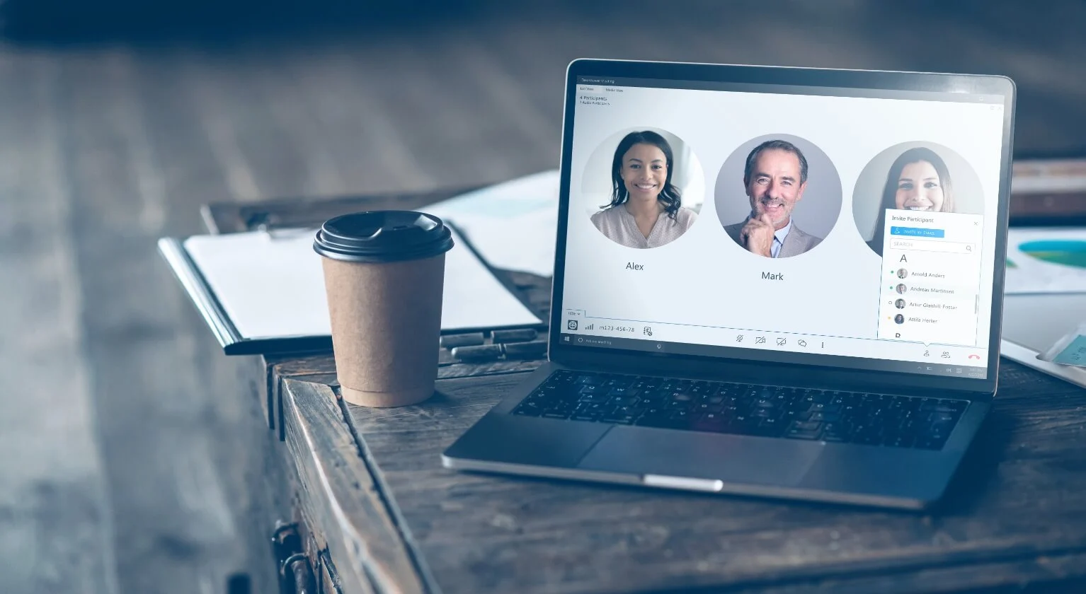 图片展示了一台笔记本电脑屏幕，上面是一个视频会议界面，有两个微笑的人物头像，旁边是一杯咖啡和一些文件。