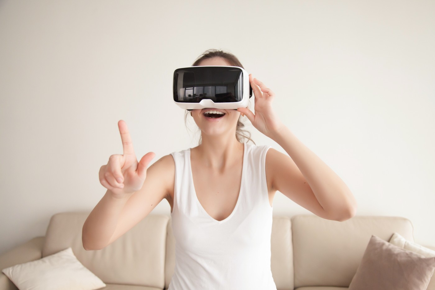 图片中是一位女士穿着白色无袖上衣，戴着虚拟现实头盔，伸出手指，似乎正在体验或操作虚拟现实内容。