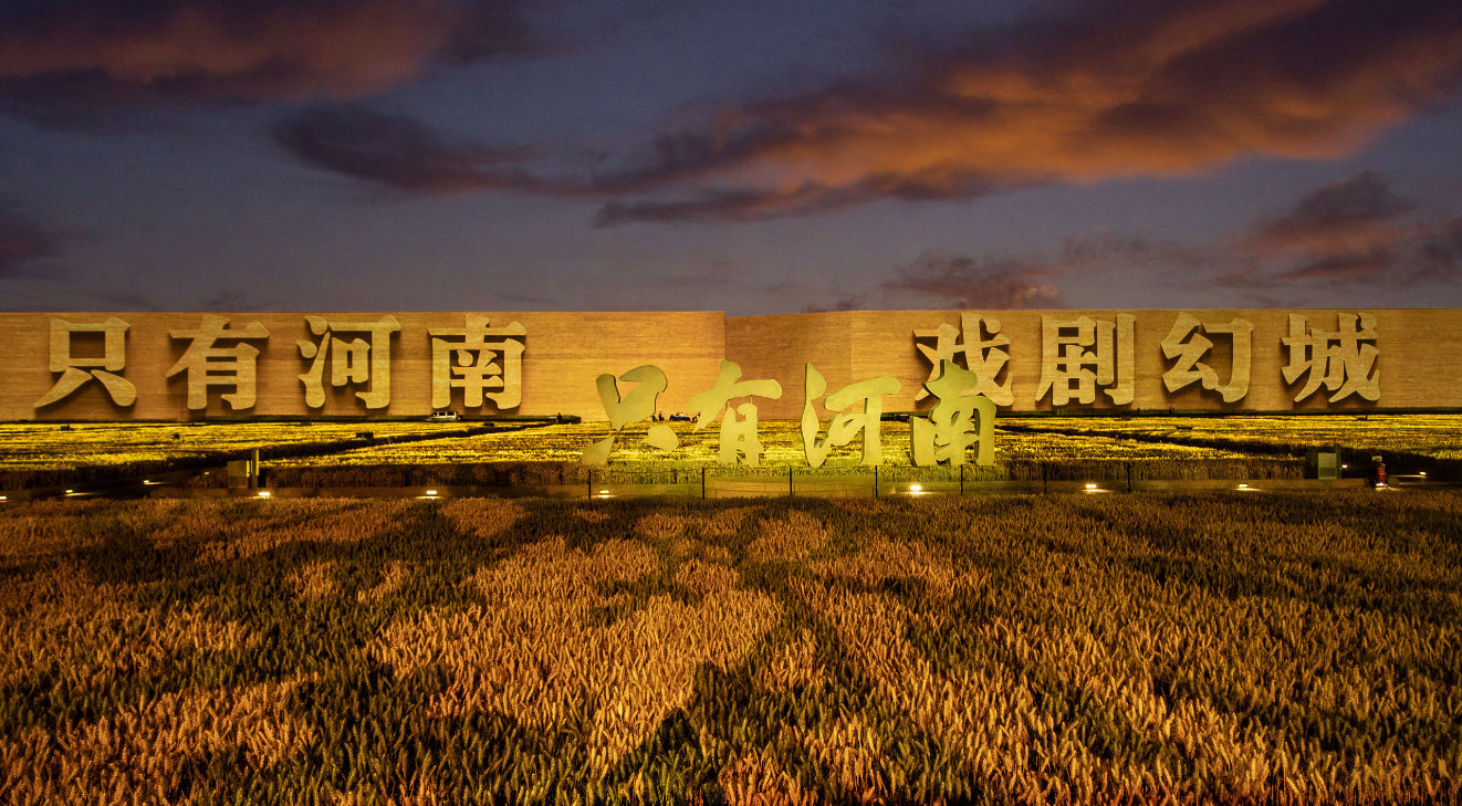 图片展示了一座建筑物，在傍晚火烧云的映衬下，建筑物上映射着“保卫黄河”四个大字，前方是稻田。
