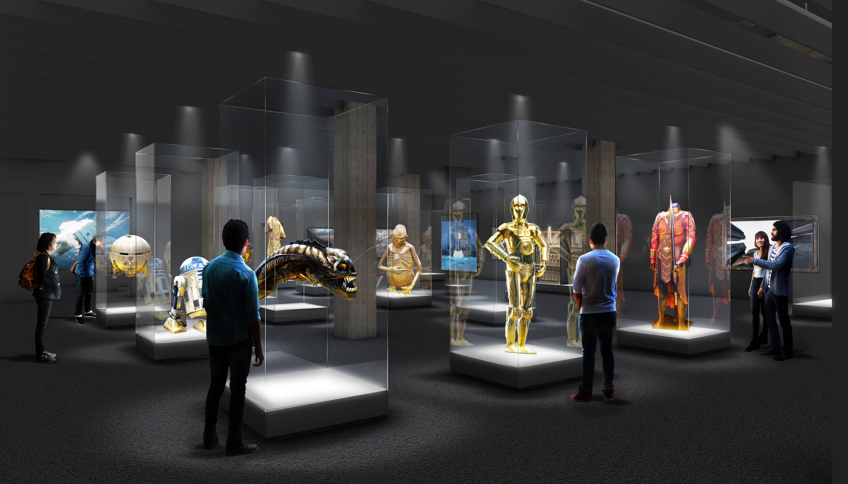 图片展示了一间展览室，里面有多个展示柜展出不同的物品，包括金色机器人模型，几位观众正在观看和讨论。