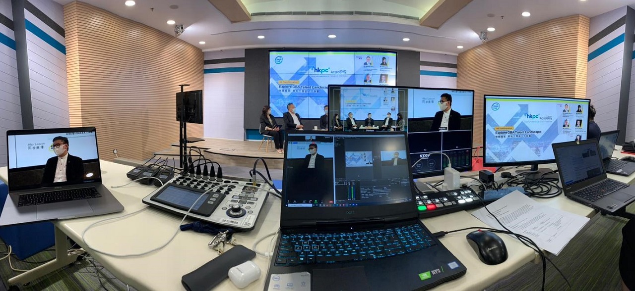 这是一张会议室内的全景照片，显示了多台电脑、屏幕，以及正在进行的视频会议，有人物参与讨论。