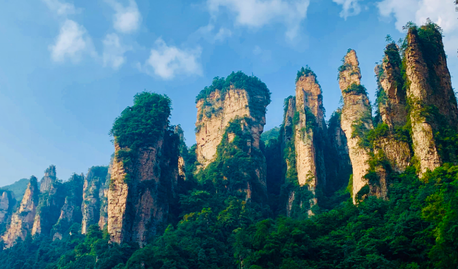 这张图片展示了壮观的石柱群，高耸入云，覆盖着绿色植被，背景是清澈的蓝天。