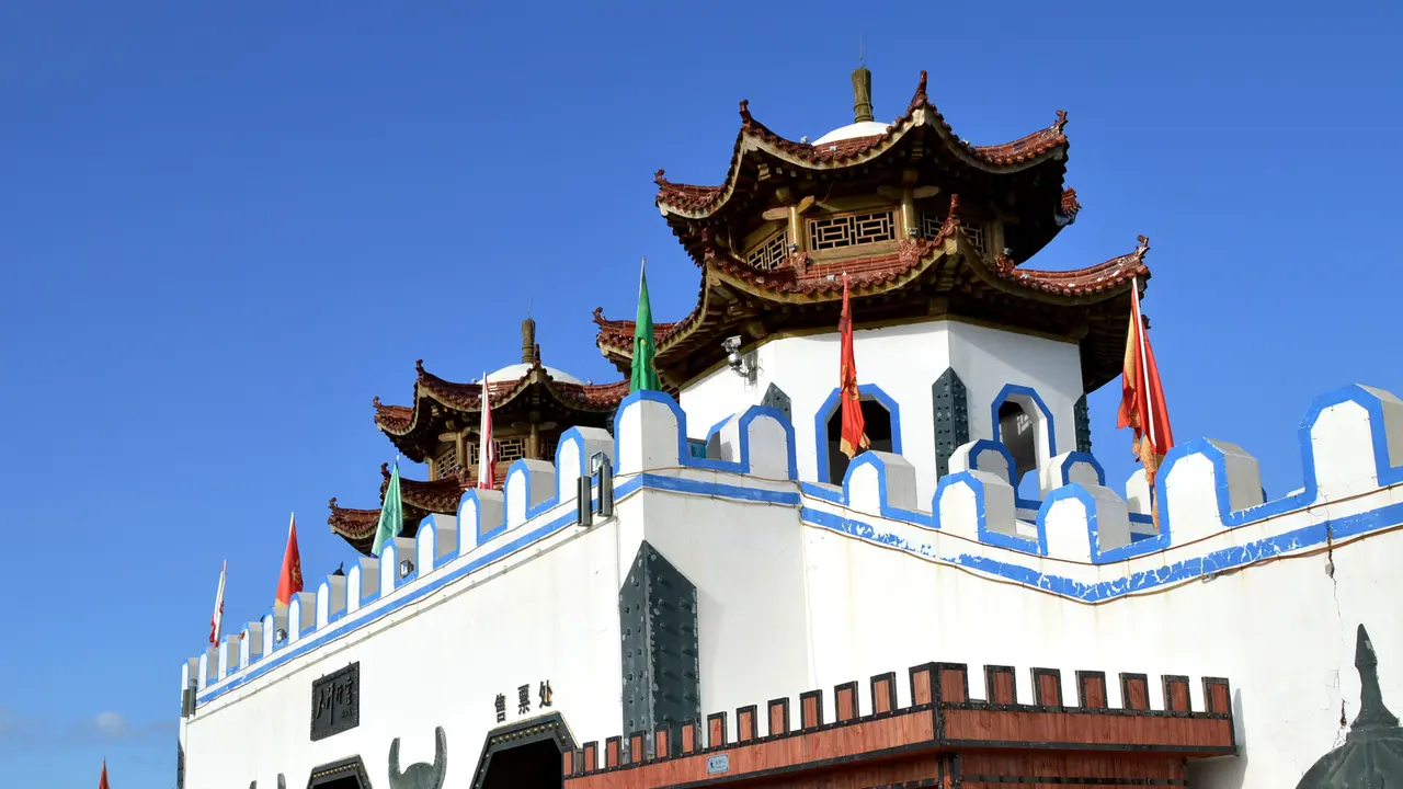 图片展示了一座具有中国传统建筑风格的建筑，蓝天下，屋顶有飞檐和宝顶，墙体为白色，飘扬着红旗。