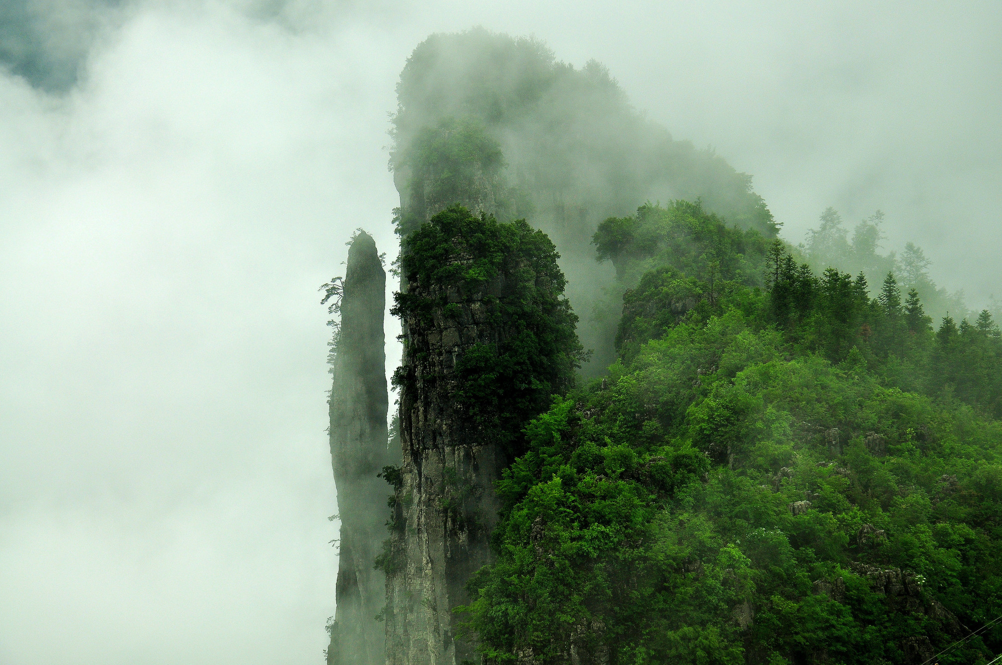 这是一张山峰云雾缭绕的照片，山峰被绿色植被覆盖，给人一种神秘莫测和自然原始之美的感觉。